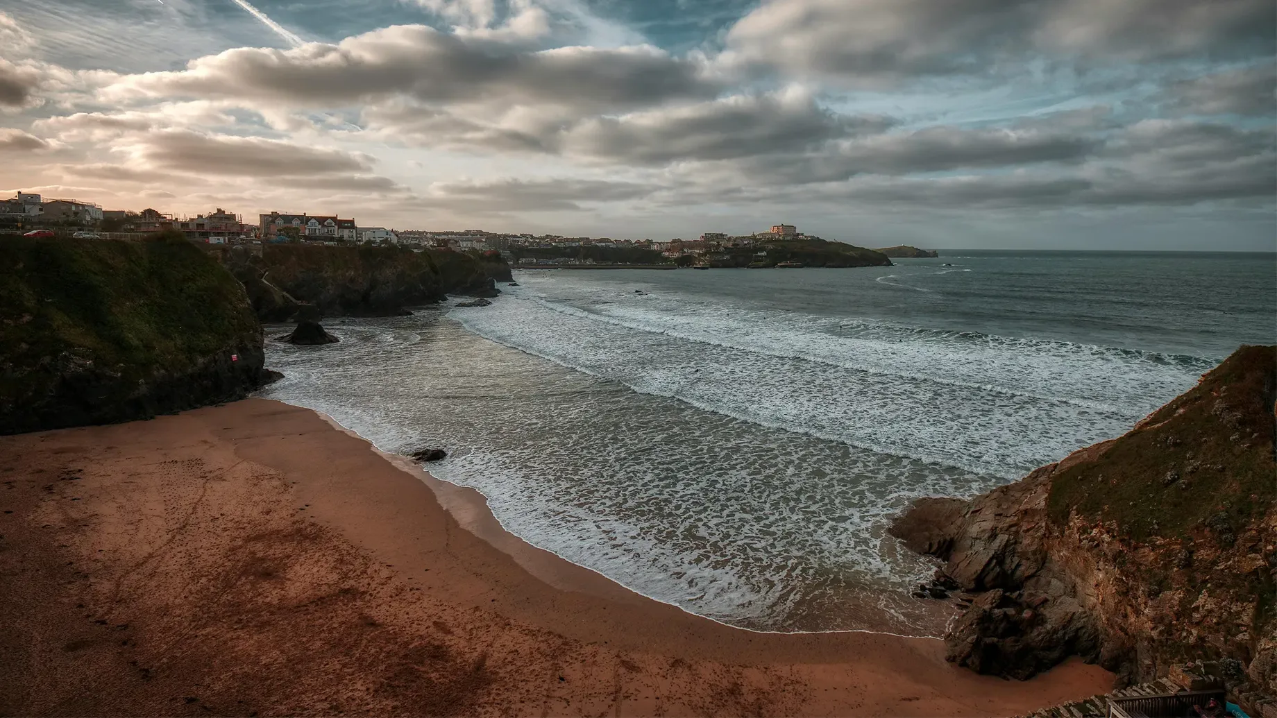 A beach with a body of water and a city in the distance.