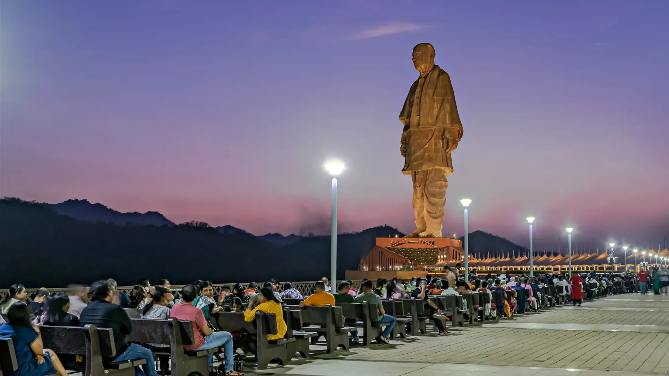 A large crowd of people sitting in front of the Statue of Unity in India