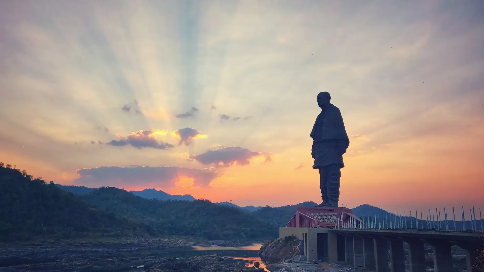 A statue of a person on a bridge with a sunset in the background.