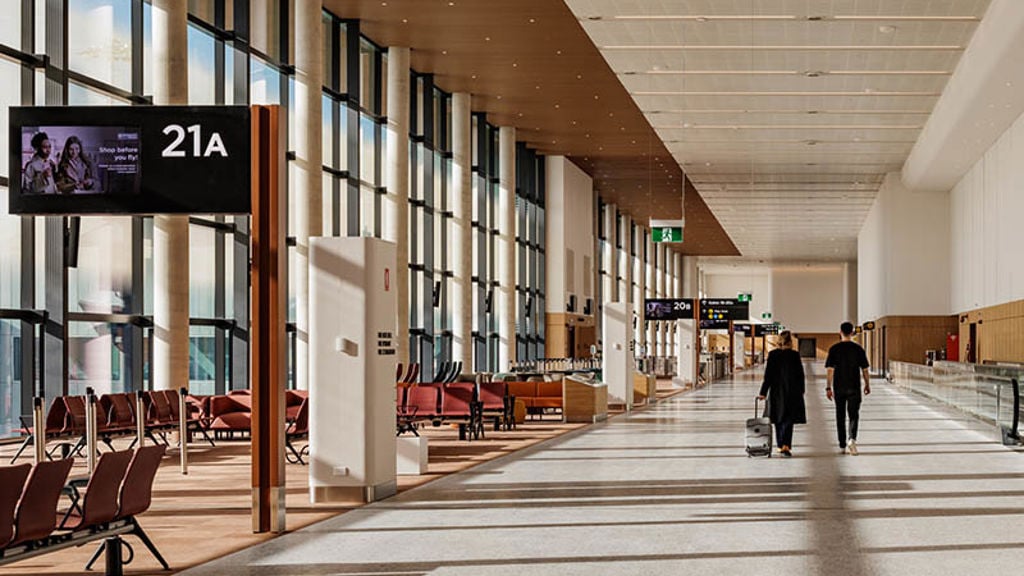 A couple of people walking past a gate lounge at the airport